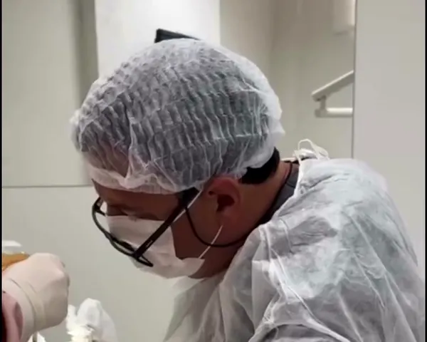 Dr. Dgiovanini, de touca e máscara, durante uma cirurgia de implante, com o kit cirúrgico na bancada